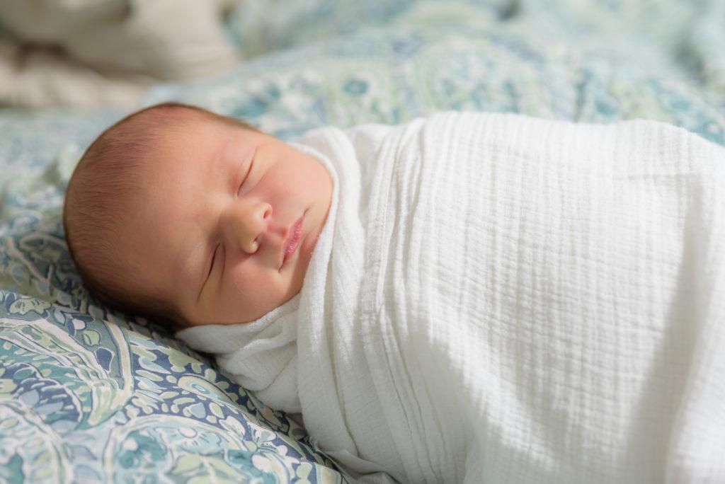 Owen as a newborn, swaddled in white and sleeping.