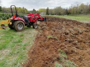 A red tractor turns over fresh dirt to prepare for planting.